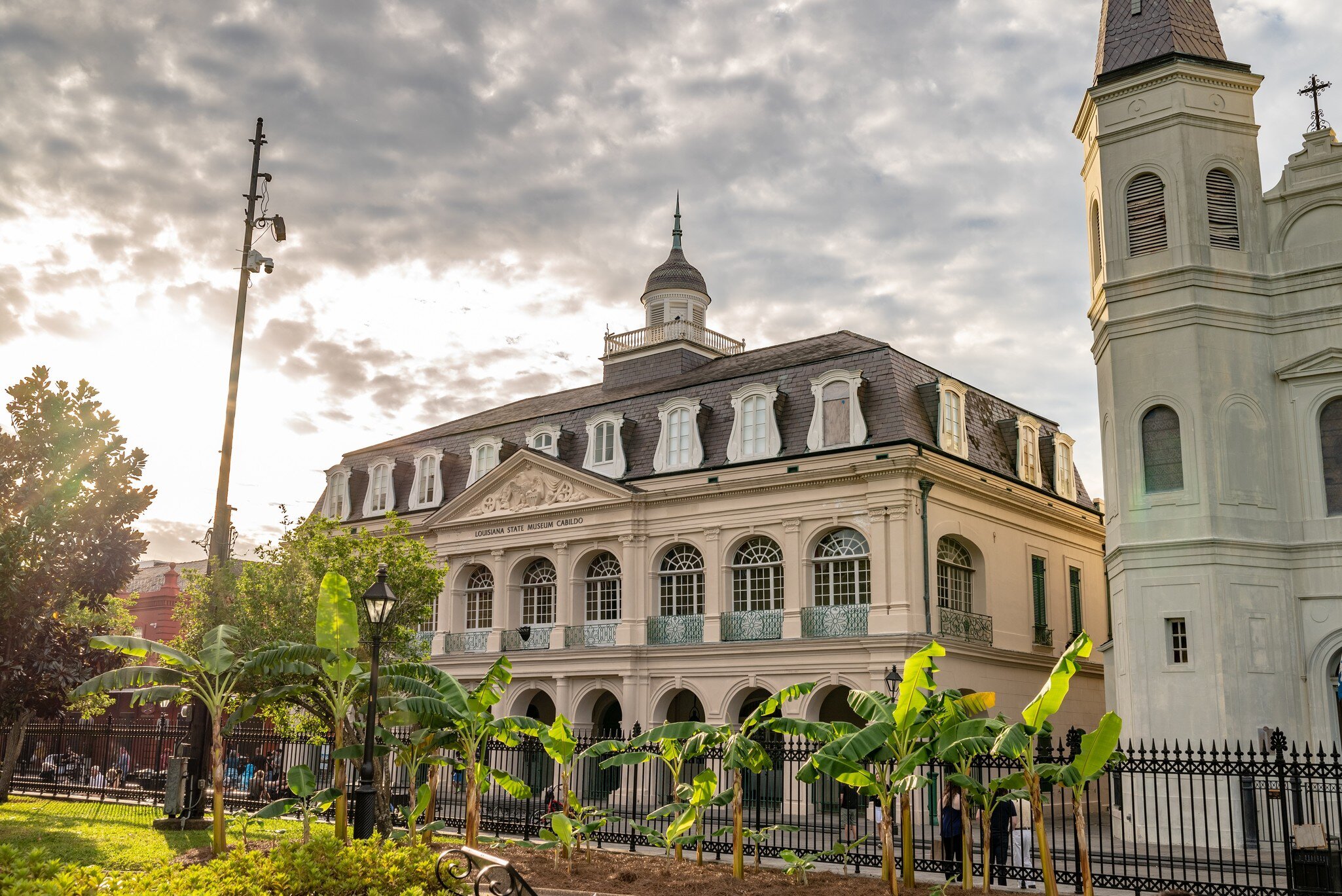 A historic building with arched windows and a mansard roof graces a city square.