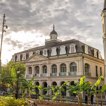 A historic building with arched windows and a mansard roof graces a city square.