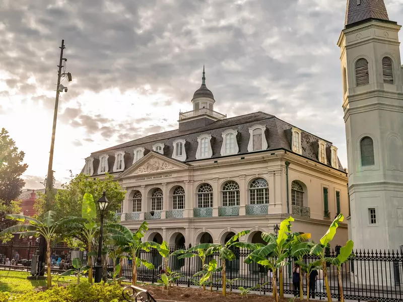 New Orleans, LA - October 26, 2021: The iconic Cabildo (Louisiana State Museum) in view at sunset in Jackson Square, in the French Quarter, with banana trees in the foreground., License Type: media, Download Time: 2025-02-27T11:56:29.000Z, User: gwencotter, Editorial: true, purchase_order: 56530 - Guidebooks, job: Global Publishing-WIP, client: New Orleans 10, other: Gwen Cotter