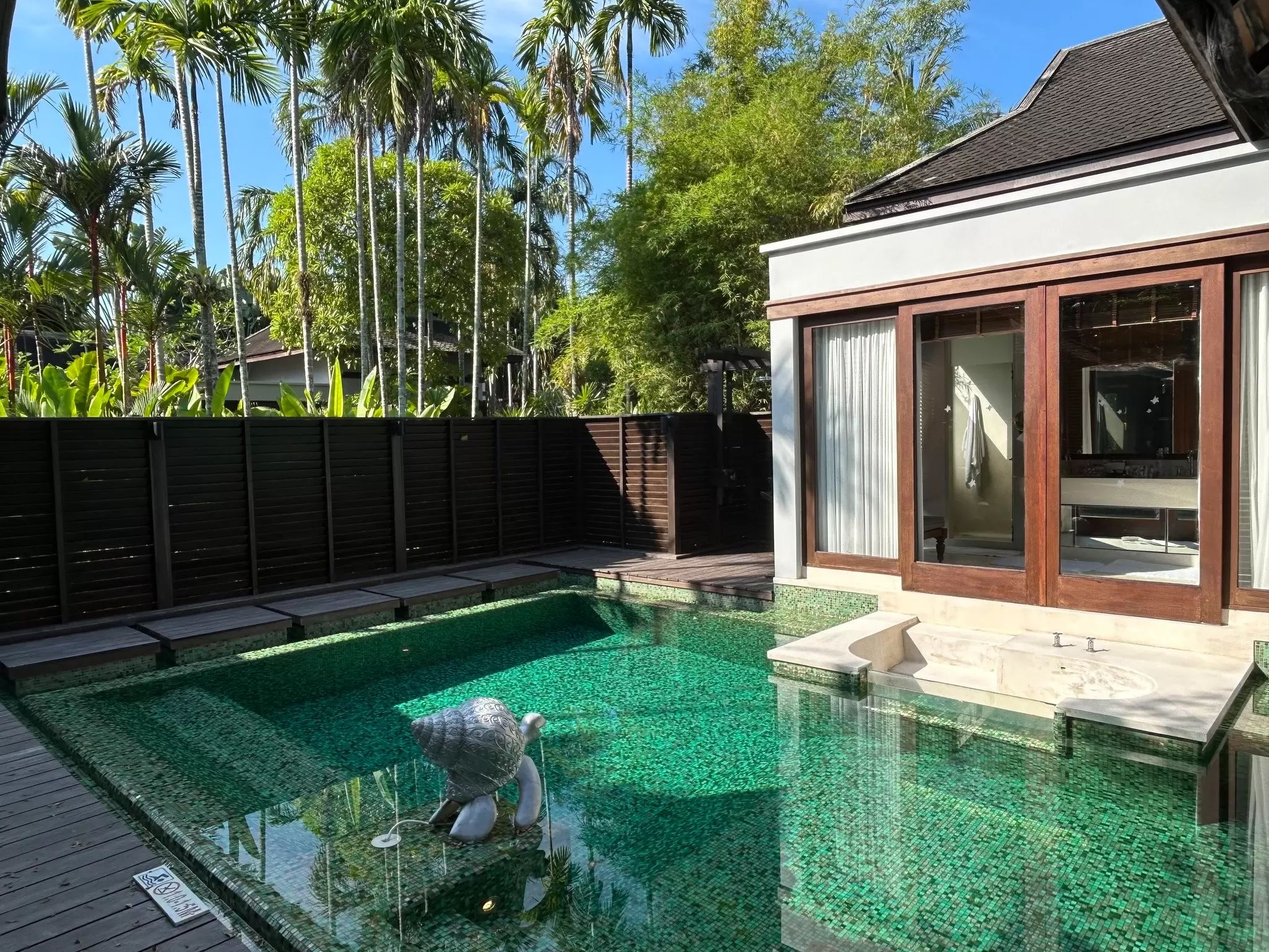 A large villa with a plunge pool surrounded by a high fence and palm trees