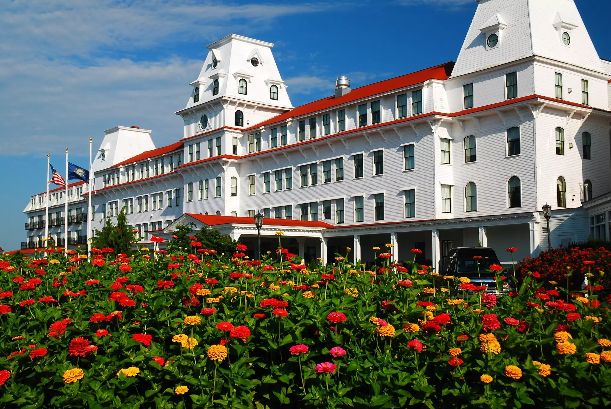 Beds of blooming flowers are seen in front of a huge, white-painted hotel.