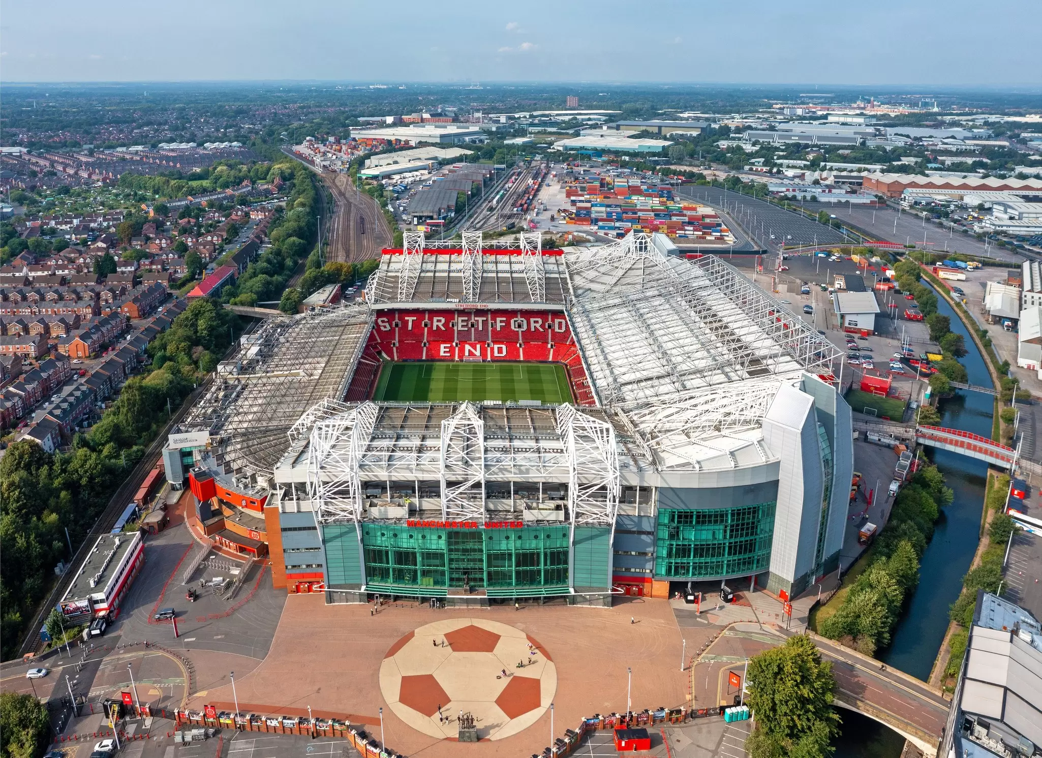 A large stadium with a central green football pitch and a series of red folding seats