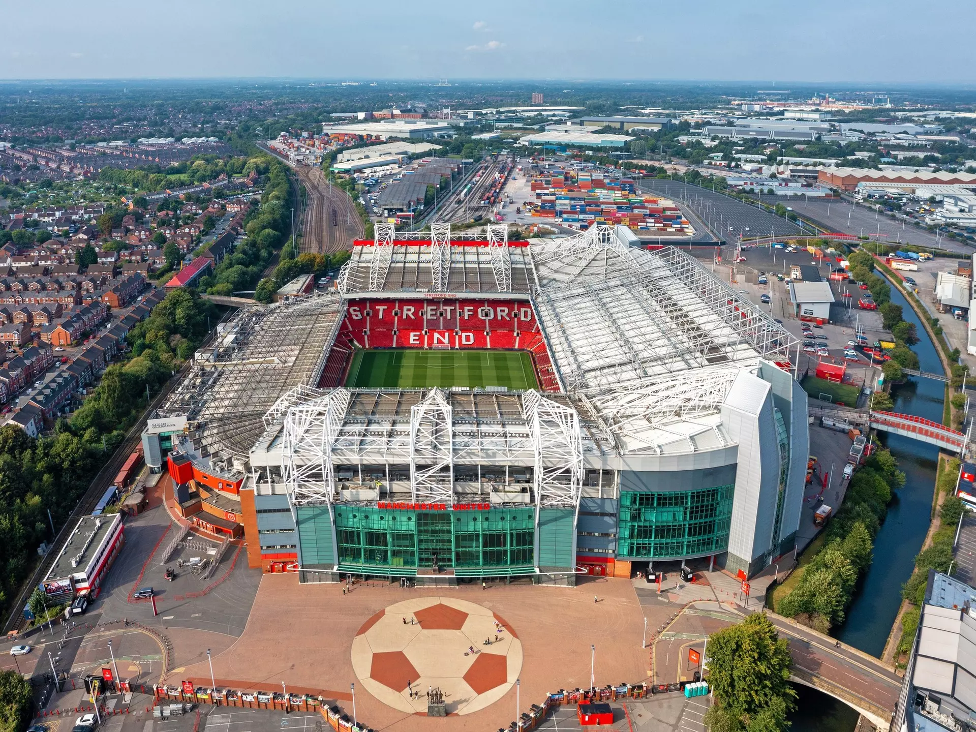 A large stadium with a central green football pitch and a series of red folding seats