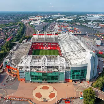 A large stadium with a central green football pitch and a series of red folding seats