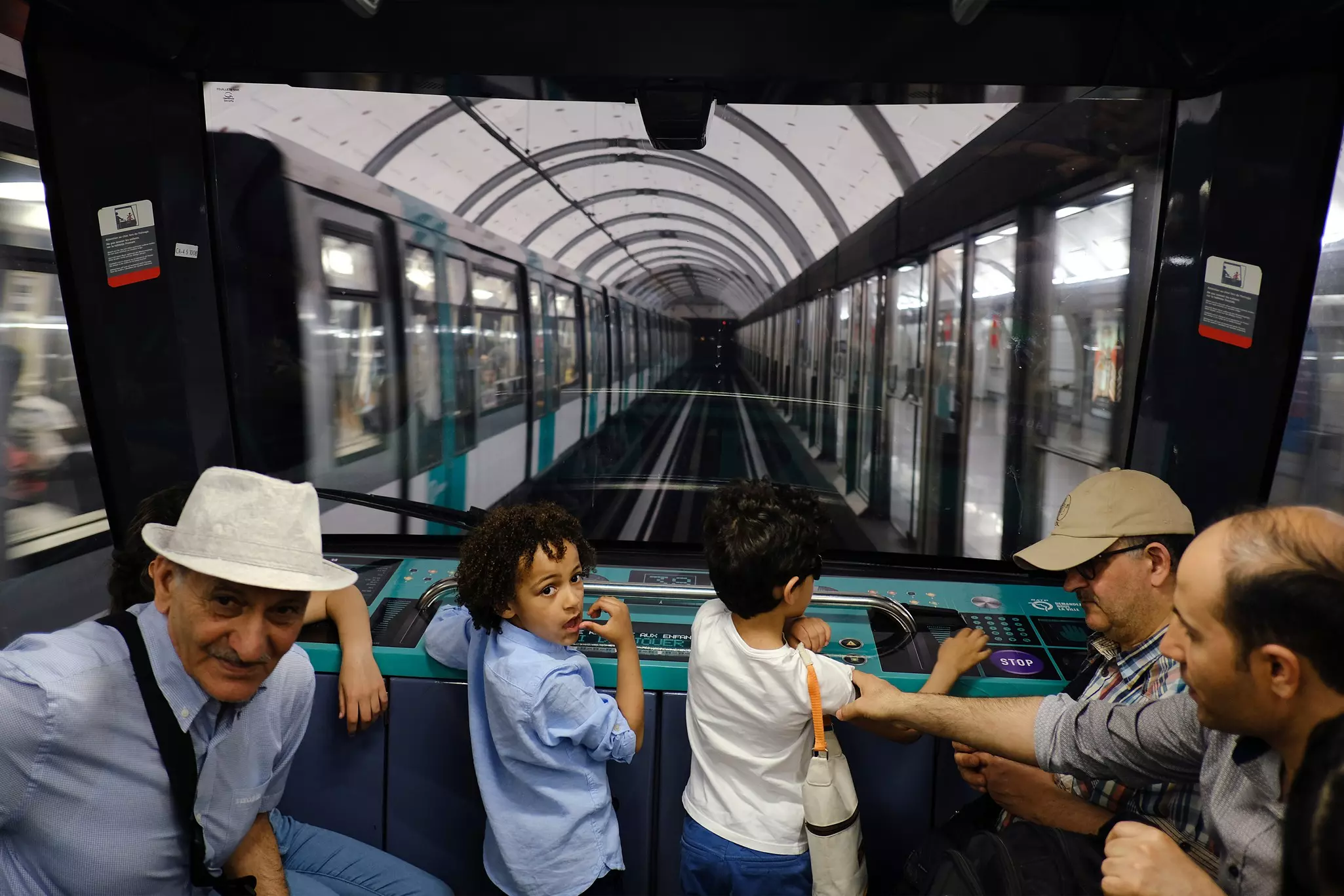 Children stand at the front of a subway car and watch the tracks through the windshield as the train pulls into a station.