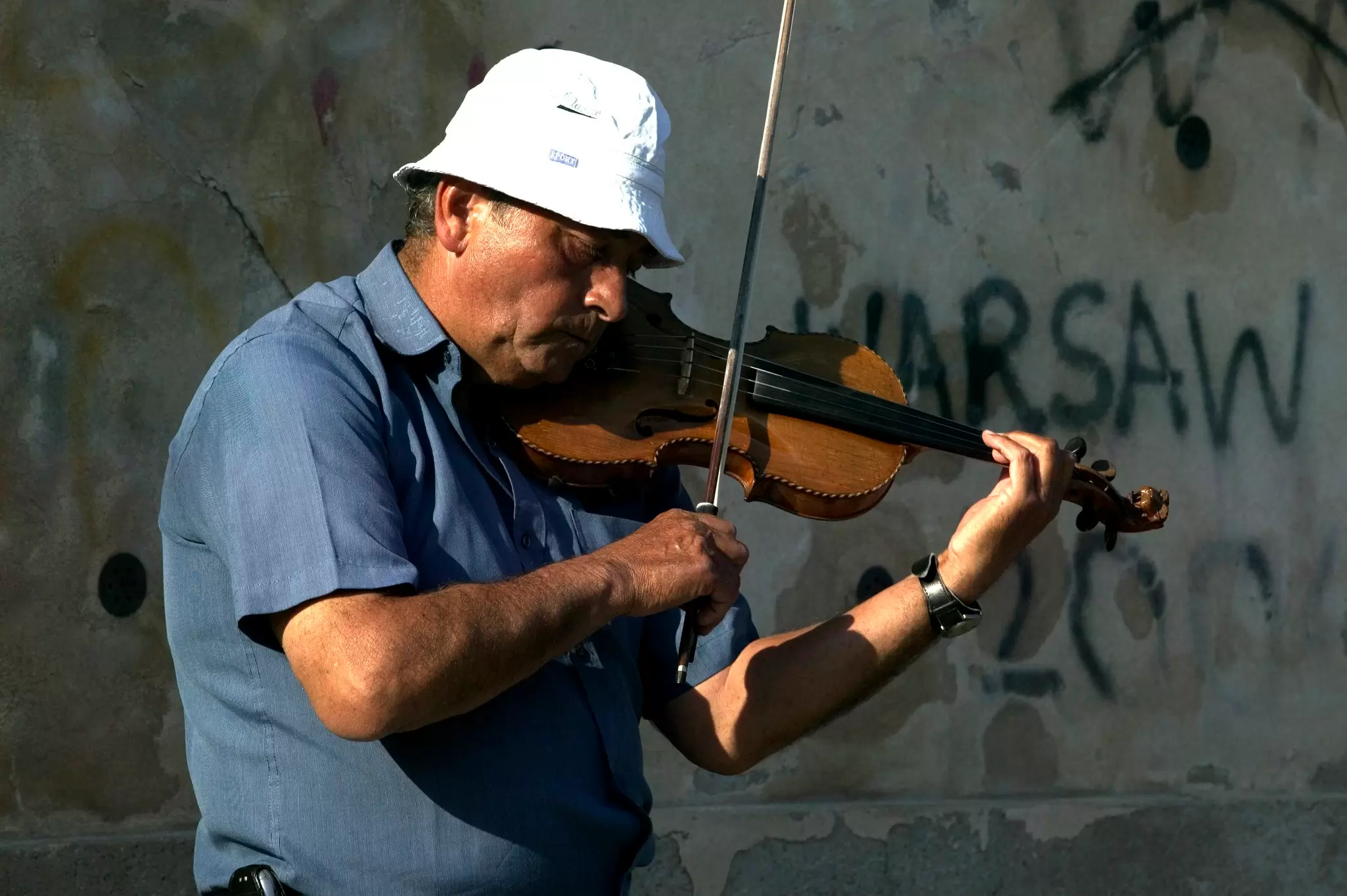 Male violinist busking in Prague by a wall with graffiti on it