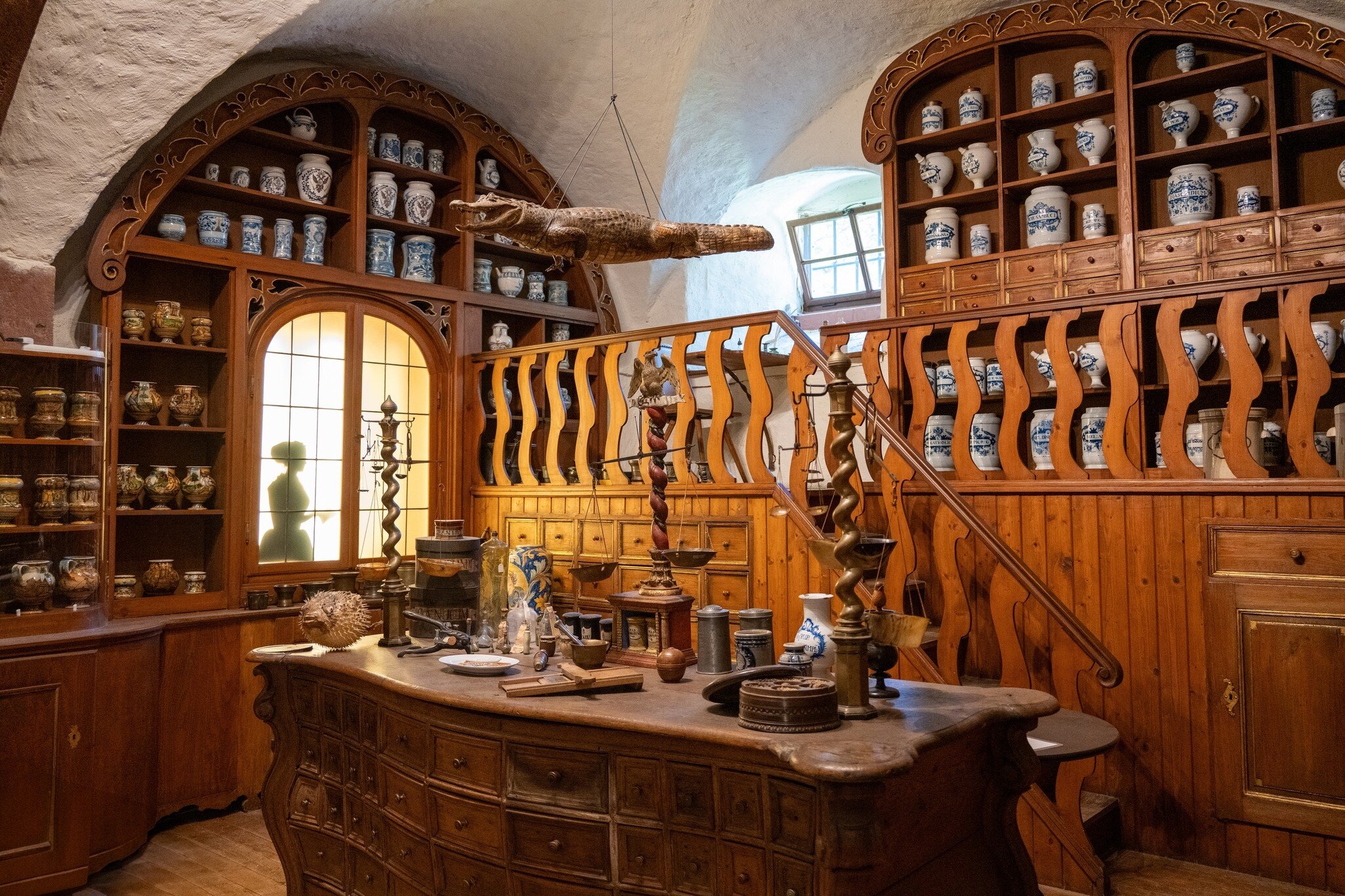 Interior of a traditional apothecary room with wooden counters, shelves and a hanging crocodile at the German Pharmacy Museum in Heidelberg, Germany.