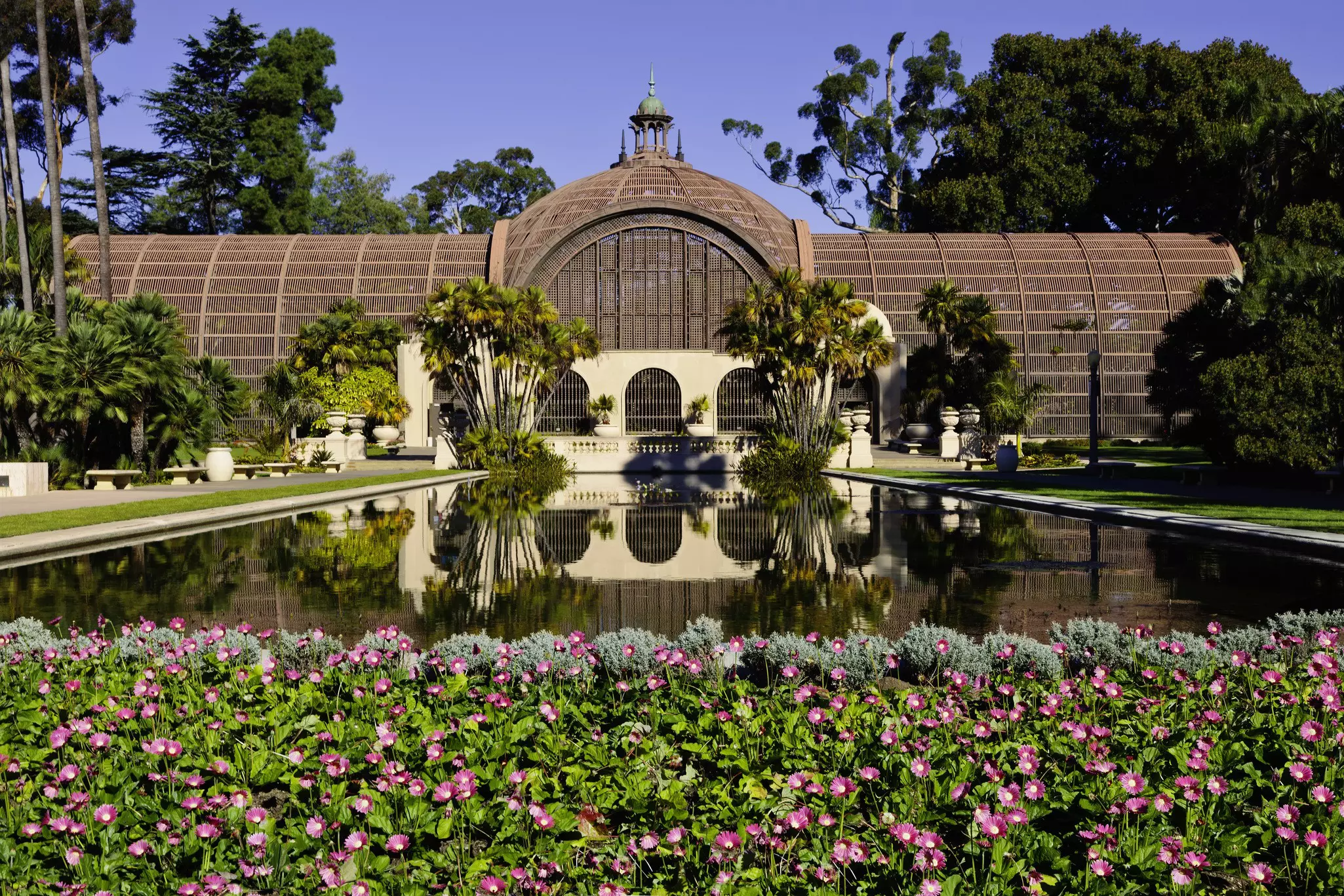 The Botanical Building in Balboa Park, San Diego reflects into a lake surrounded by flowers
