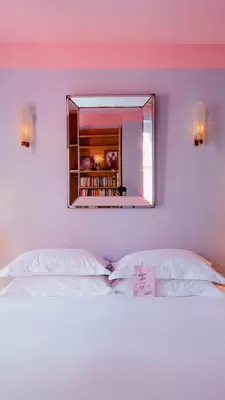 A bed with a white covering and four white pillows; lamps are on the bedside tables, and the wall behind the bed is lavender.