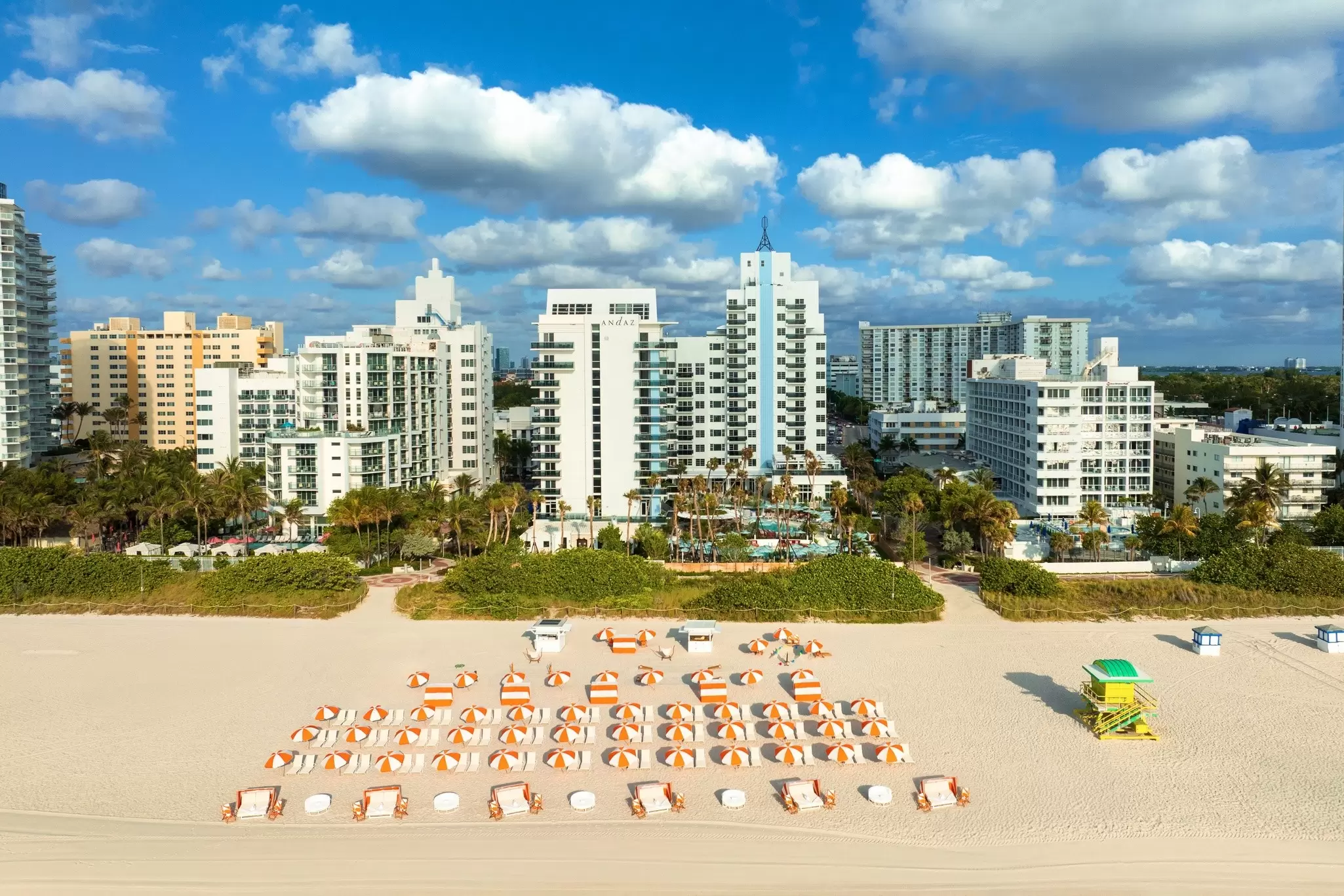 A beach with a neat row of sunloungers backed by a tall hotel; the Andaz Miami Beach