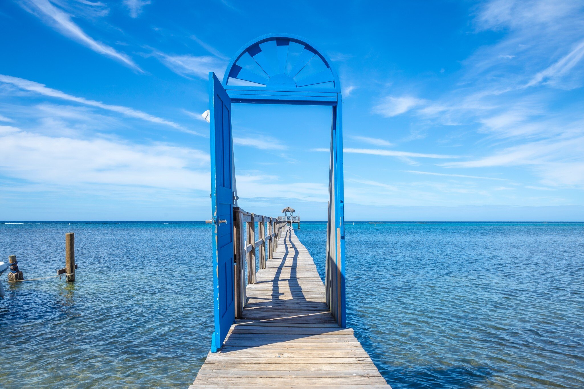 Freestanding blue door frames a wooden pier stretching over clear Caribbean water at Sandy Bay, Roatán, Honduras