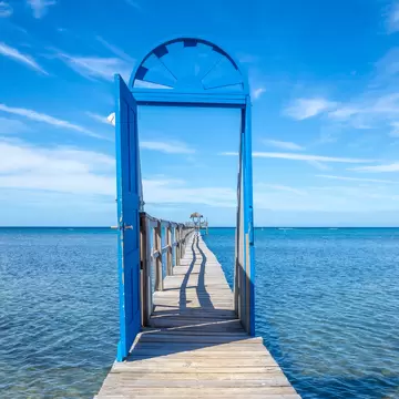 Freestanding blue door frames a wooden pier stretching over clear Caribbean water at Sandy Bay, Roatán, Honduras