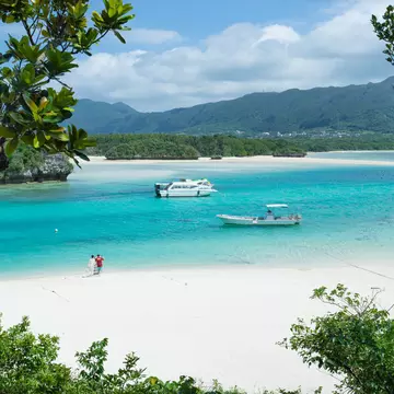 Two small boats moored in a peaceful turquoise lagoon at the edge of white sands on a tropical island. 