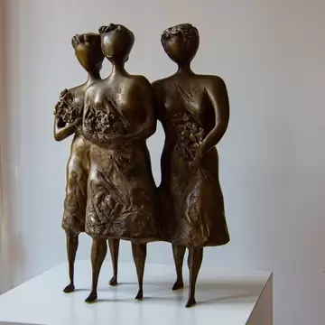 Bronze sculpture of three women holding flowers on a white plinth against a pale wall in a Chișinău gallery