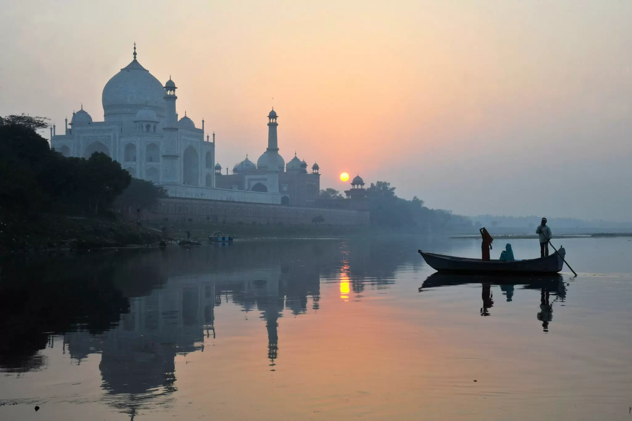 Boat paddling past Taj Mahal on Yamuna River.