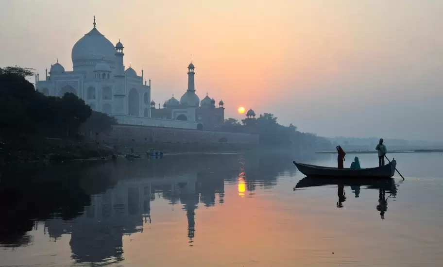 Boat paddling past Taj Mahal on Yamuna River.