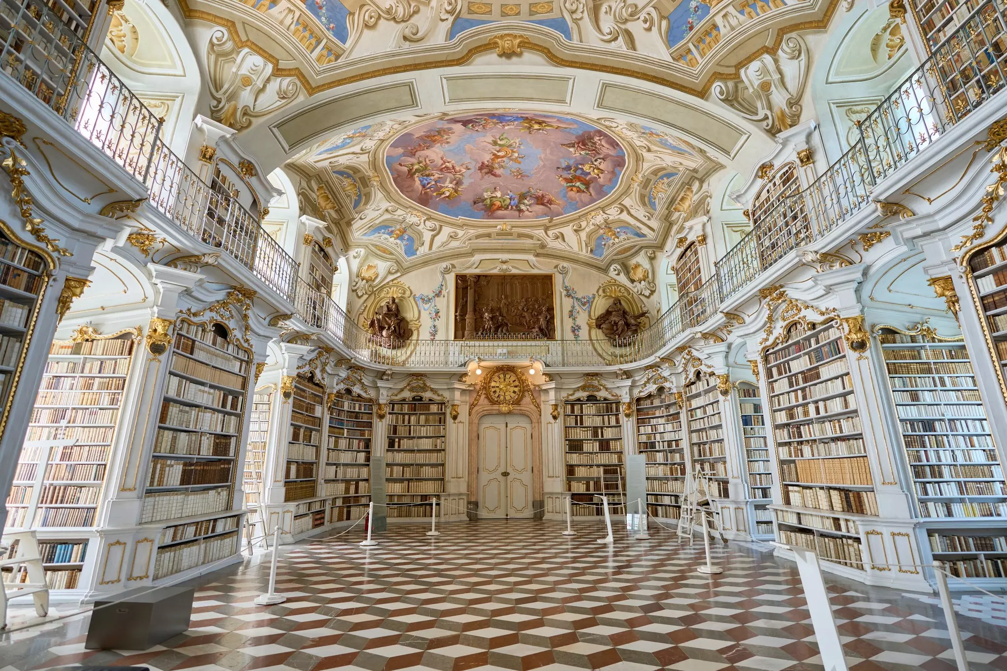 Tiled floors, shelves lined with books and an ornately painted ceiling covered in frescoes in a grand library