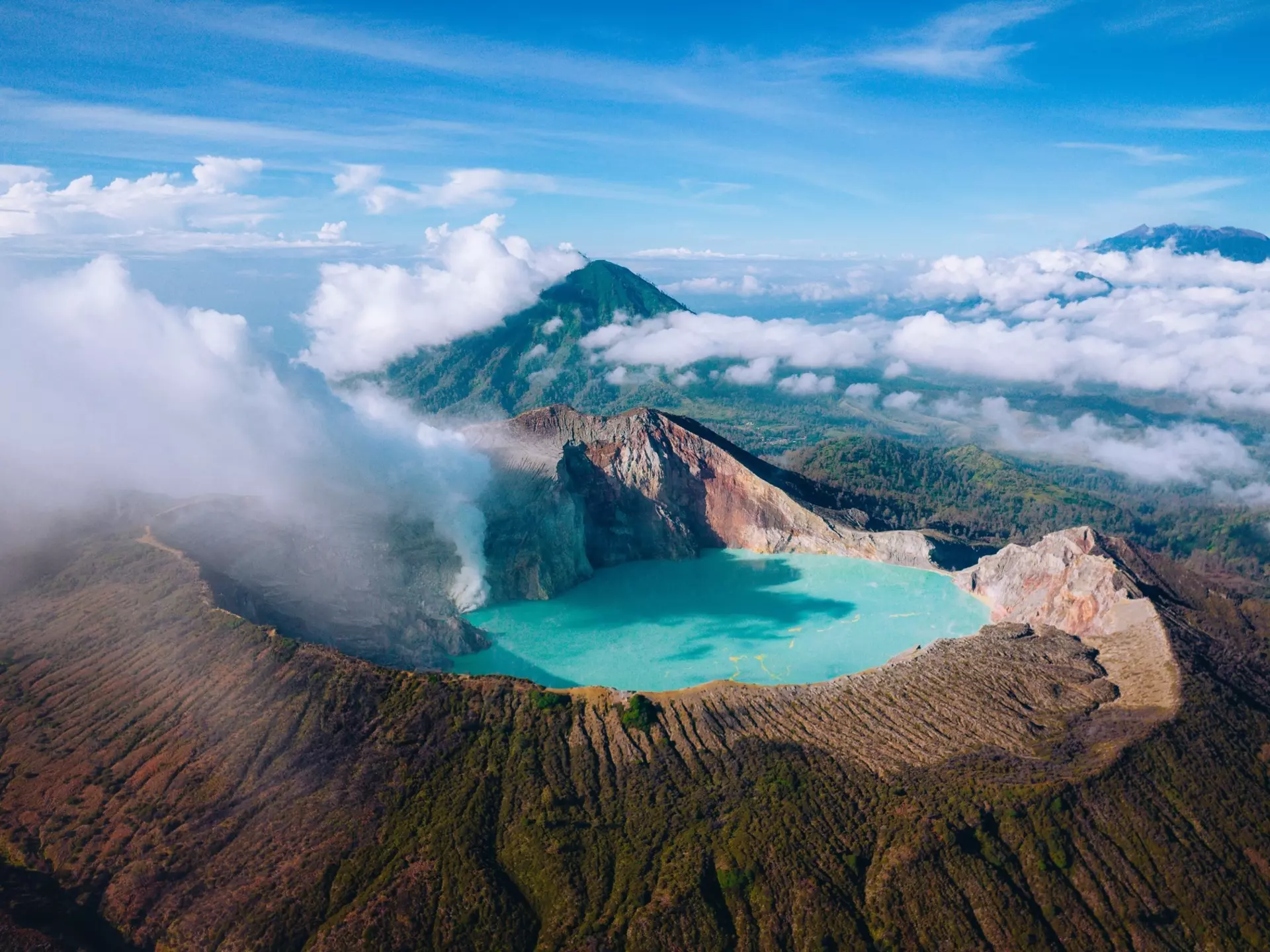 A turquoise lake in a volcanic caldera at high altitude with clouds and surrounding mountain peaks