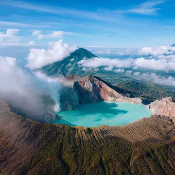 A turquoise lake in a volcanic caldera at high altitude with clouds and surrounding mountain peaks