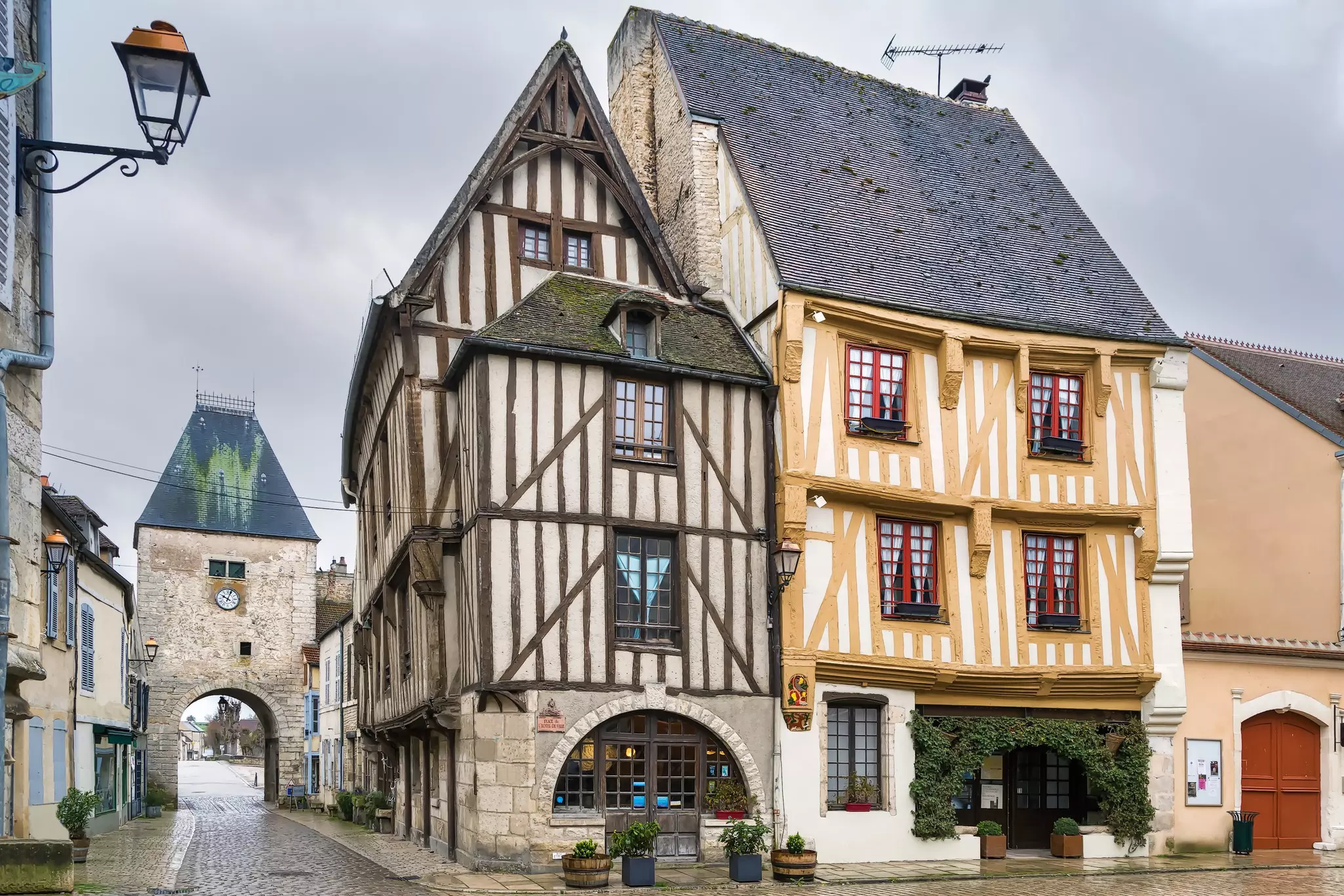 An ancient stone gateway beside two half-timbered houses in a small medieval town.