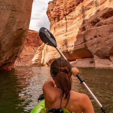 A person kayaks through a canyon of reddish rock.