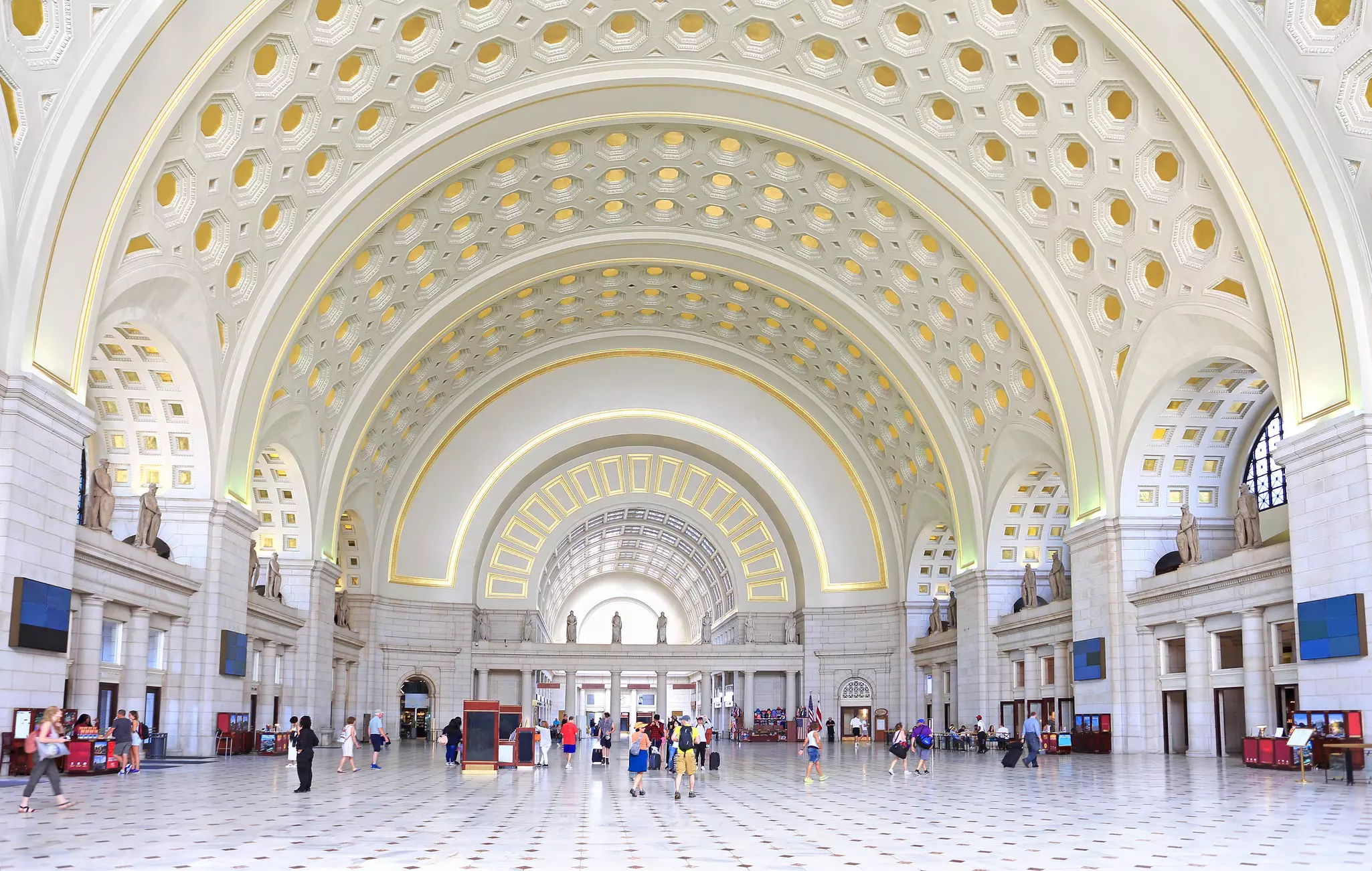 The stark white interior of a large train station with an arched ceiling.