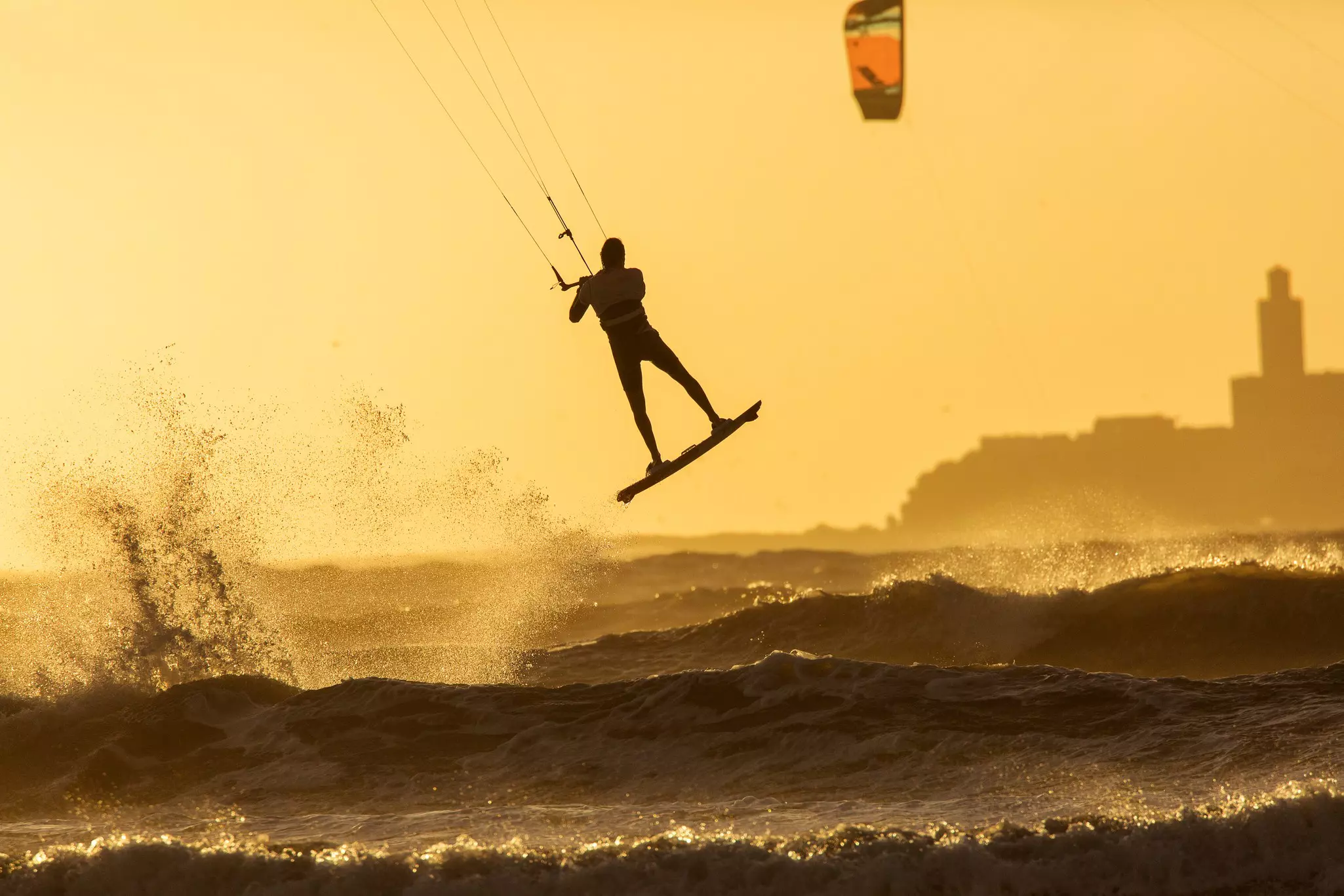 Silhoutte of kitesurfers enjoying big waves at sunset in Essaouira, Morocco. Beautiful landscape in background