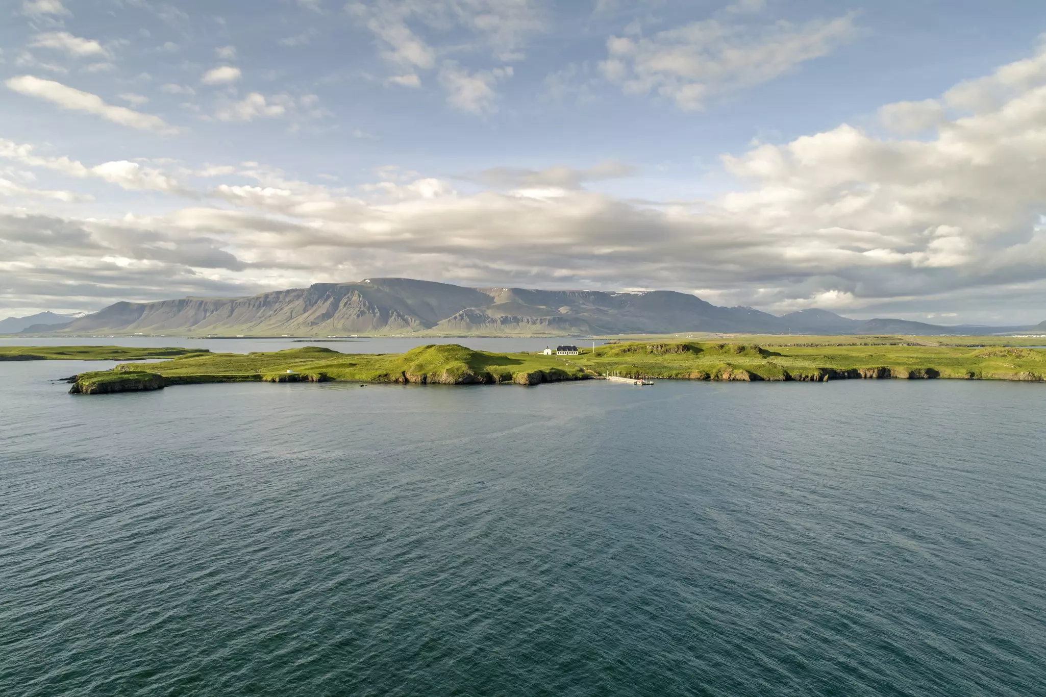 A green island in the middle of a body of water with a mountain in the background under a pale blue sky