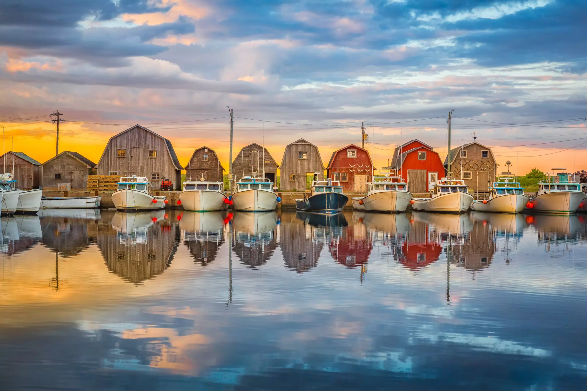 Boats docked in a small harbor with wooden huts standing in a row. The light of sunset reflects off the water
