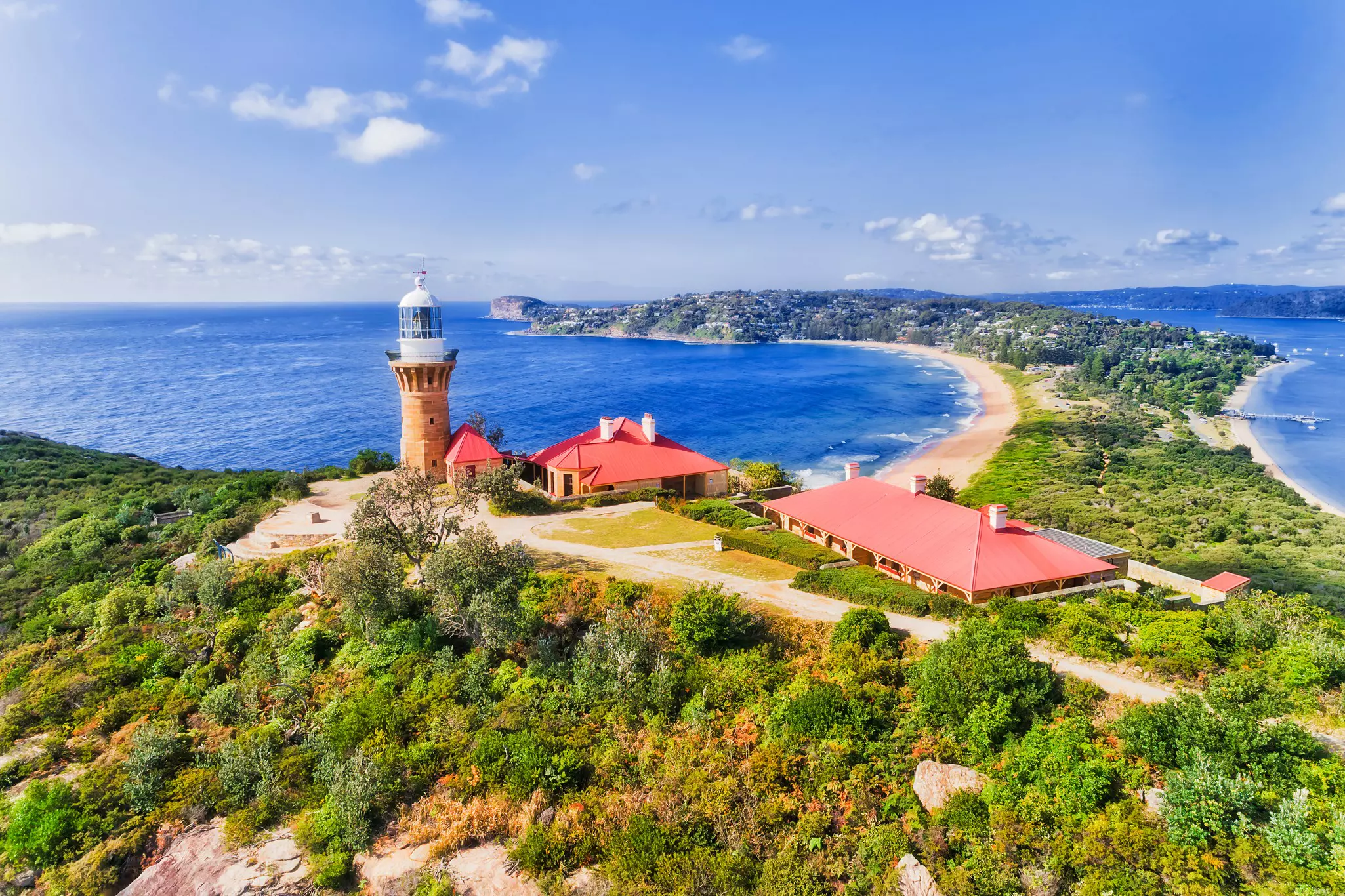 A lighthouse stands on a hill above a peninsula with sandy beaches either side of it.
