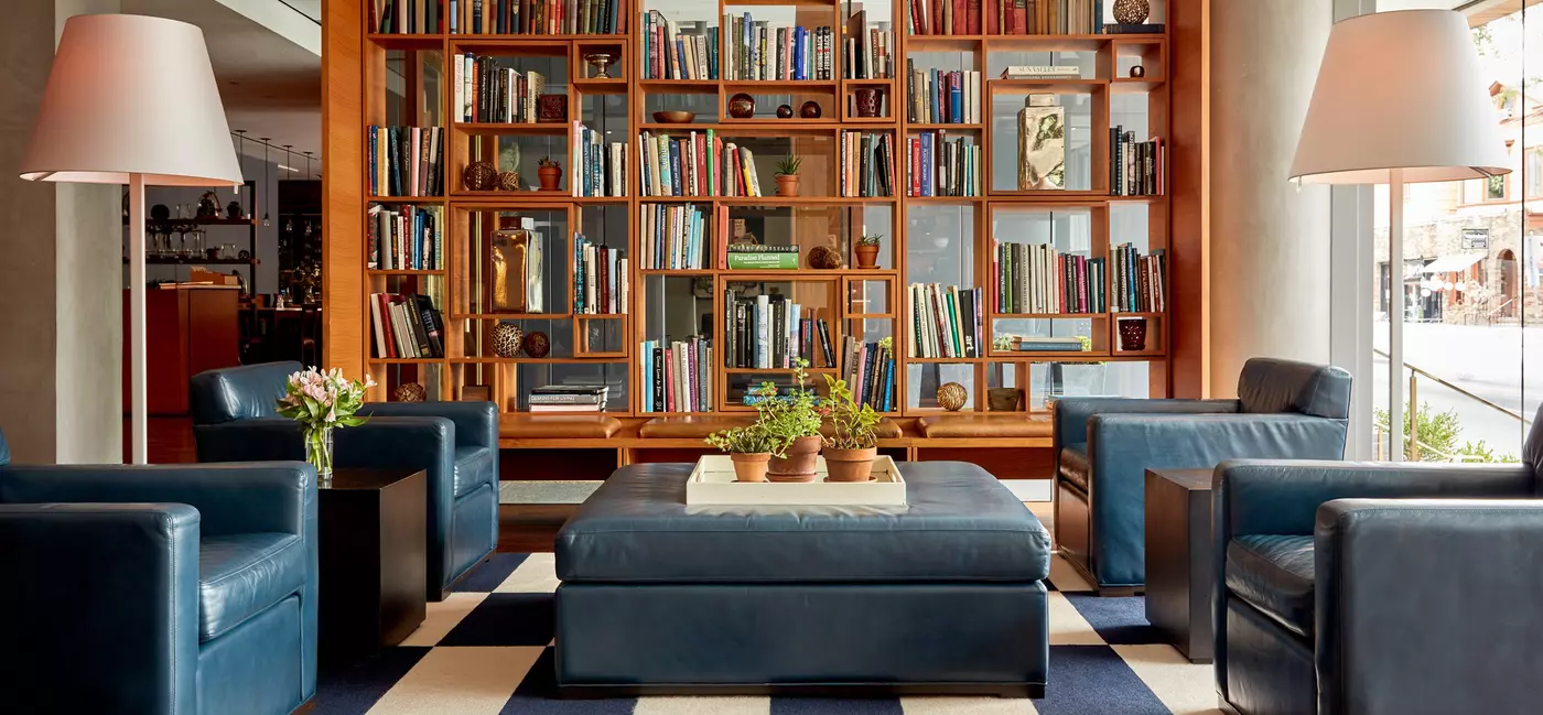 A well-stocked modern bookcase with 2 plush chairs on either side, with a coffee table in the middle
