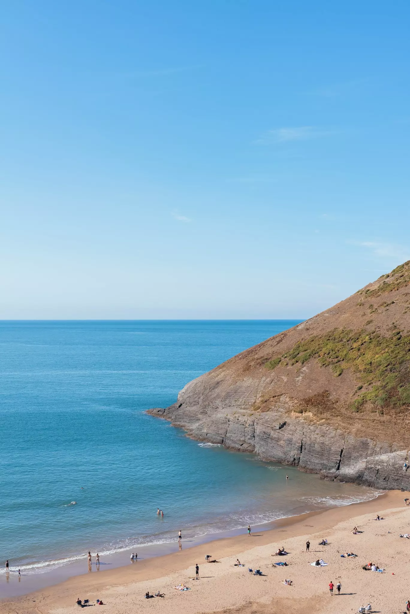 A sheltered sandy shore with people paddling in the ocean.