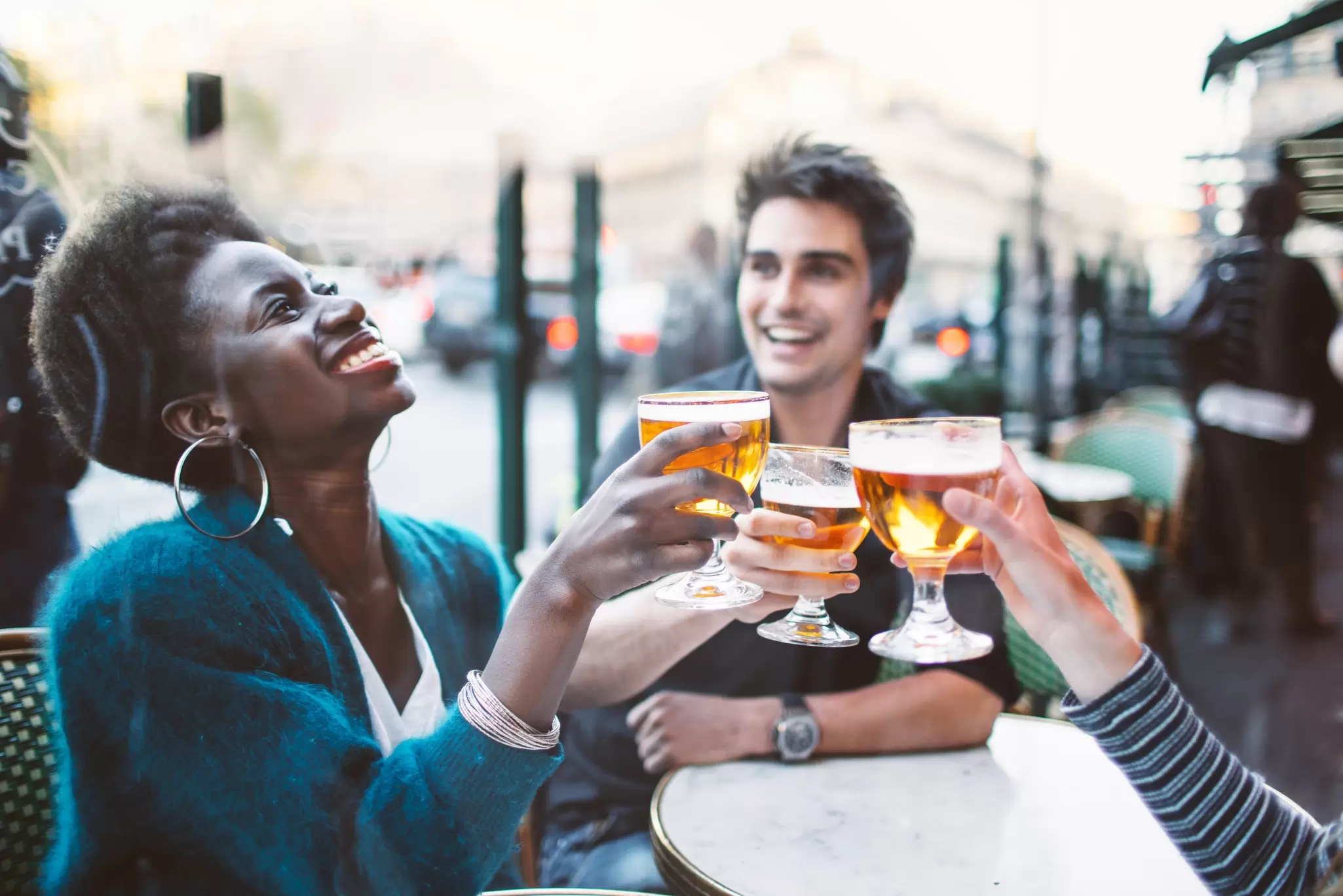Friends laughing and toasting glasses of beer at an outdoor Parisian cafe