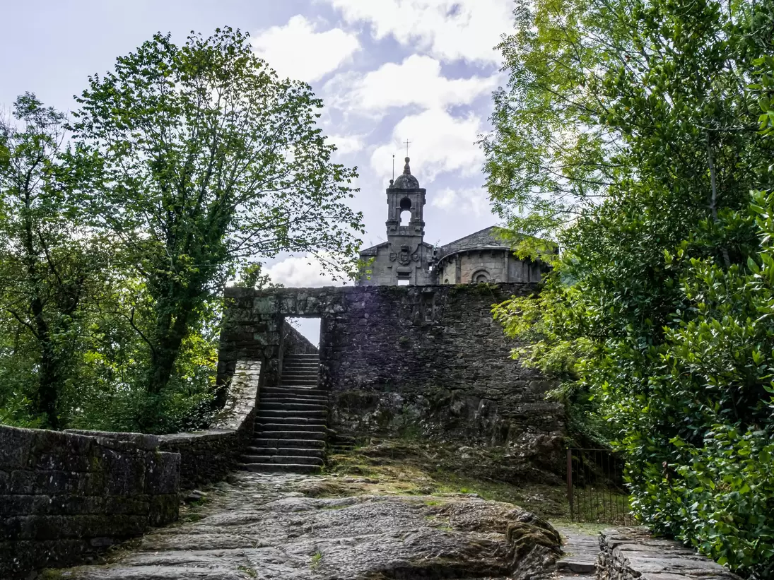 View of stone steps leading to Mosteiro de Caaveiro in Spain, framed by green trees.