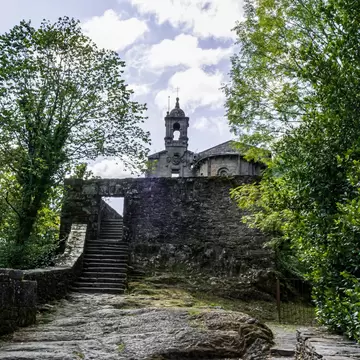 View of stone steps leading to Mosteiro de Caaveiro in Spain, framed by green trees.