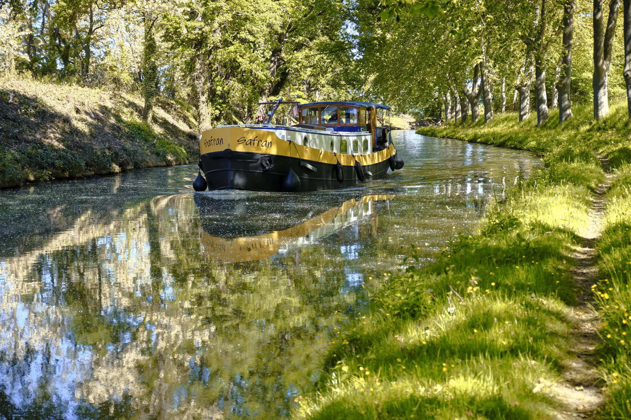 Flat boat navigating a tree-lined bend on the Canal du Midi