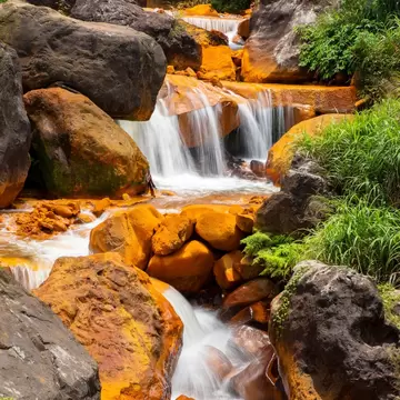 Water tumbling down golden rocks with green grass on one side at Golden Waterfall, Jinguashi.
