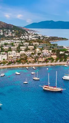 Boats float on bright blue water along a coastline covered in buildings. 