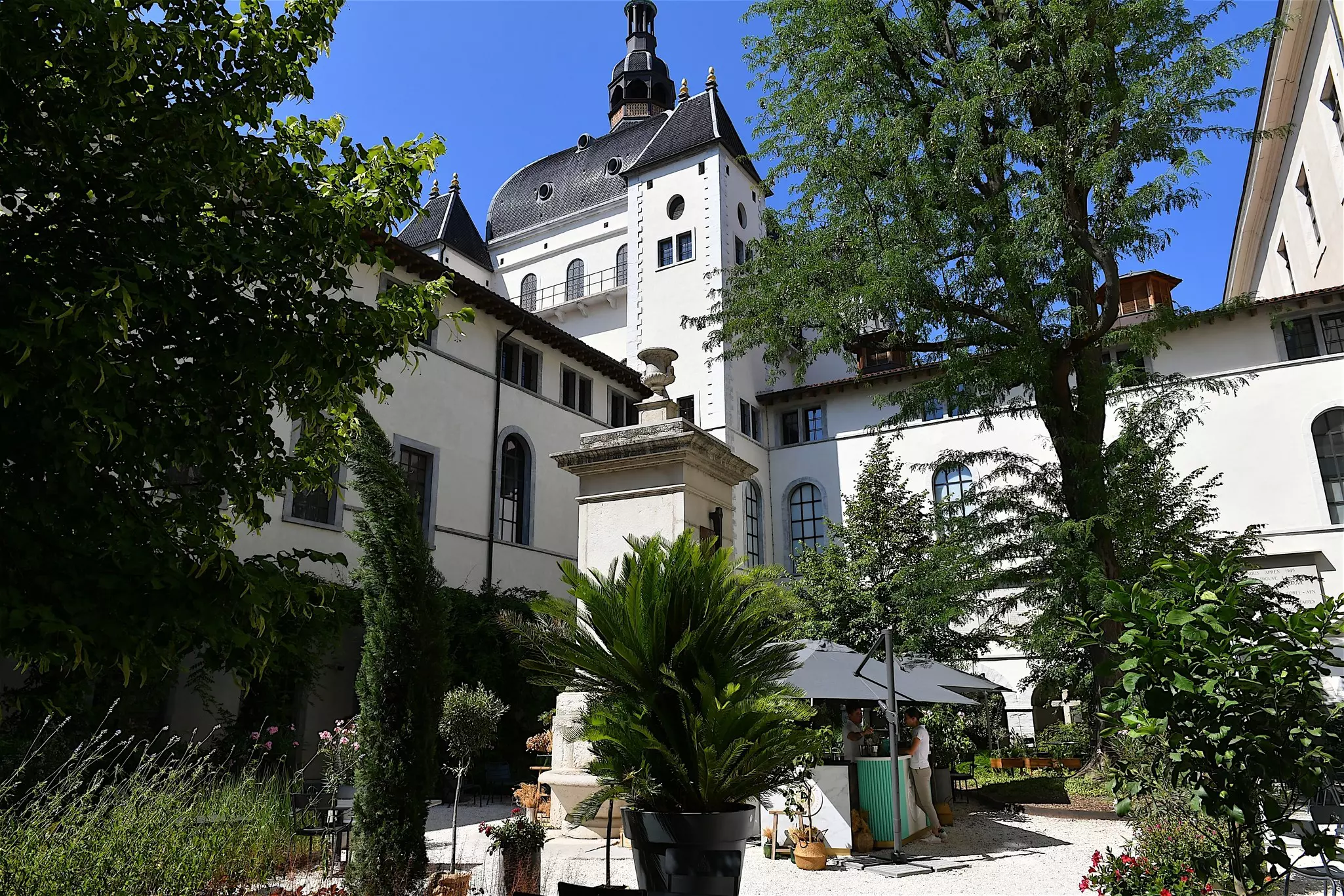 A visitor orders from a bar surrounded by trees in an inner courtyard of the former hospital Hotel-Dieu in Lyon