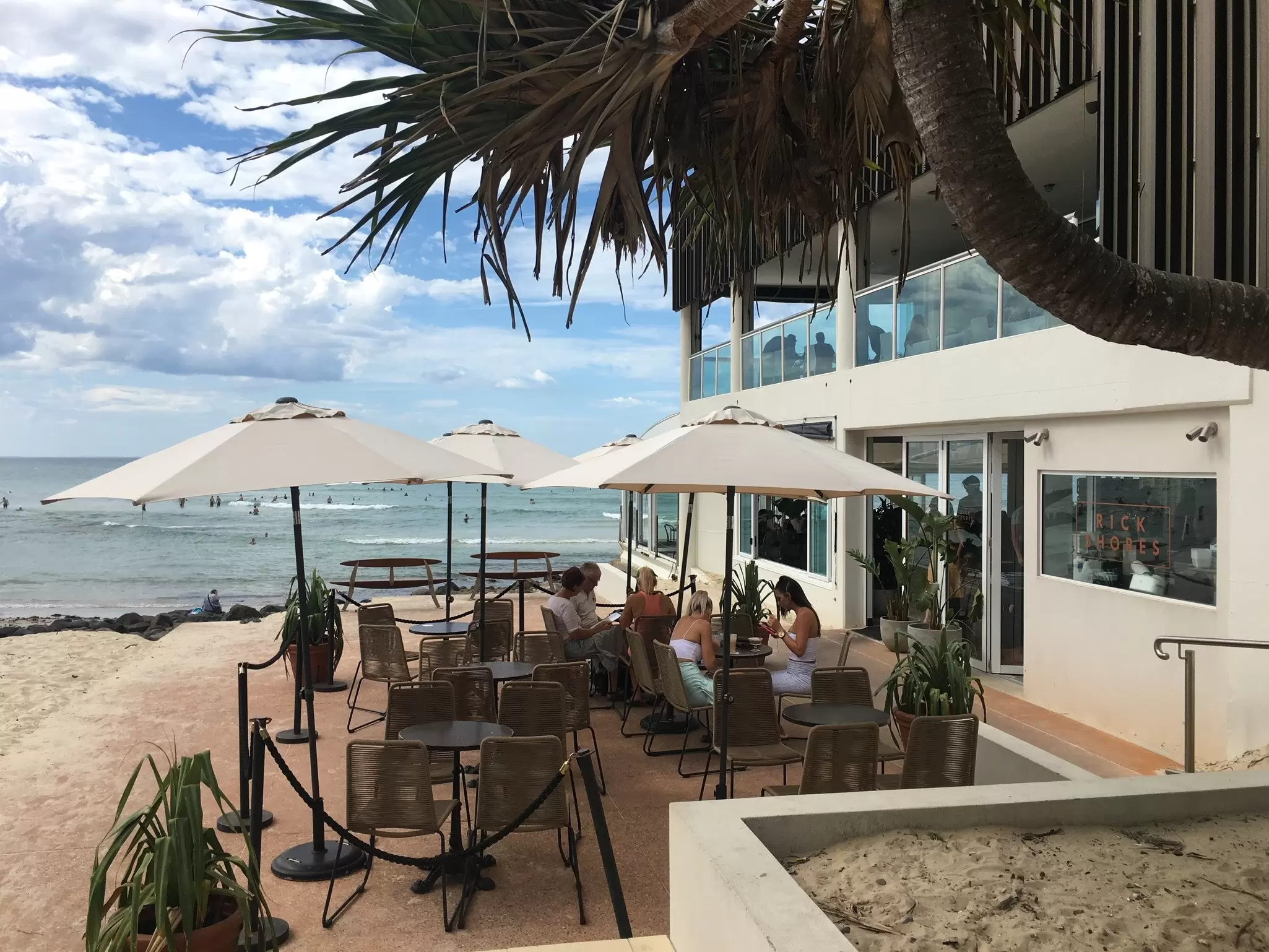 People seated at tables under umbrellas at a beachside restaurant in the Gold Coast, Queensland, Australia
