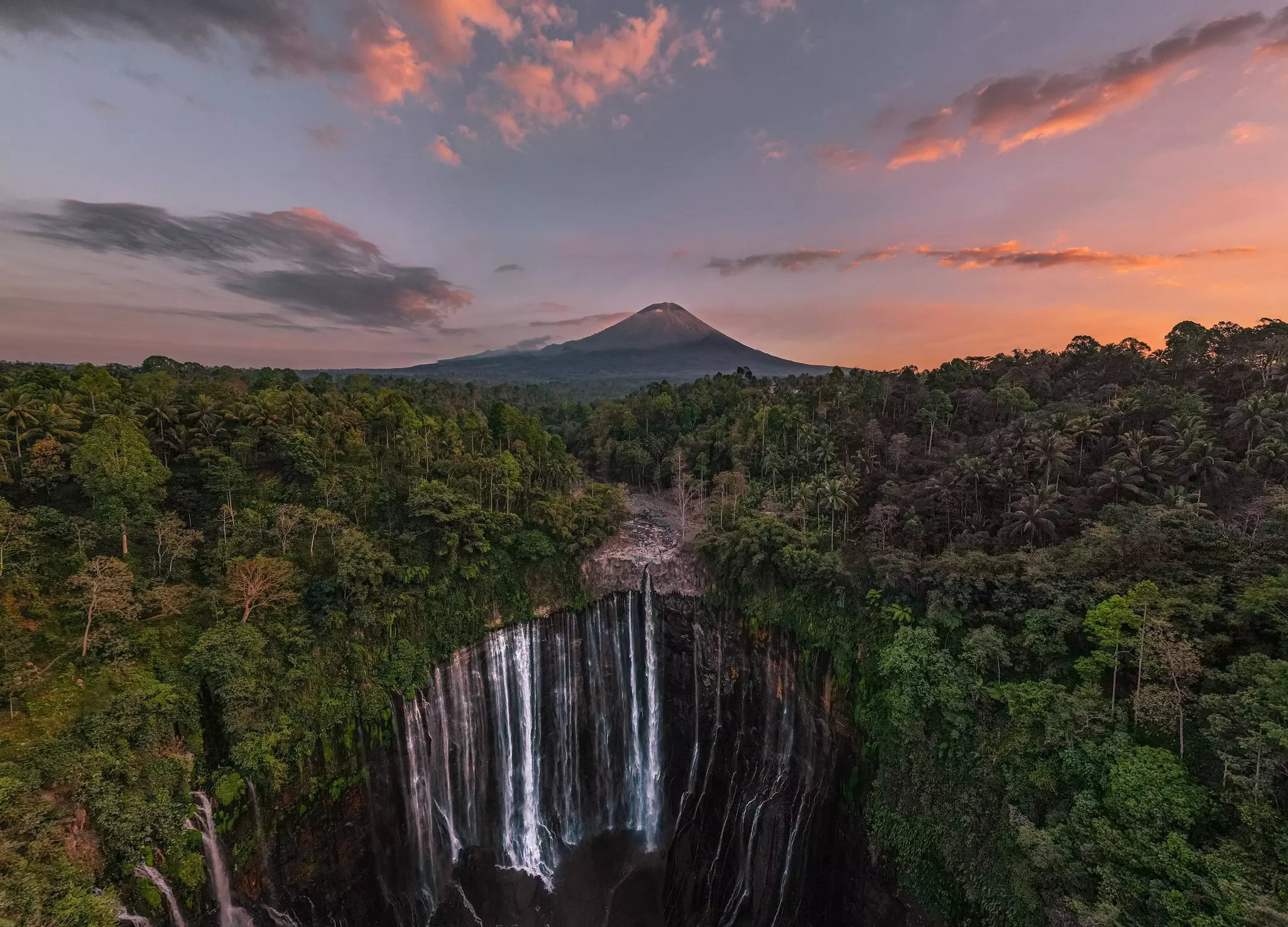 Aerial view of Tumpak Sewu waterfall at sunrise with Mount Semeru in the background, East Java, Indonesia.