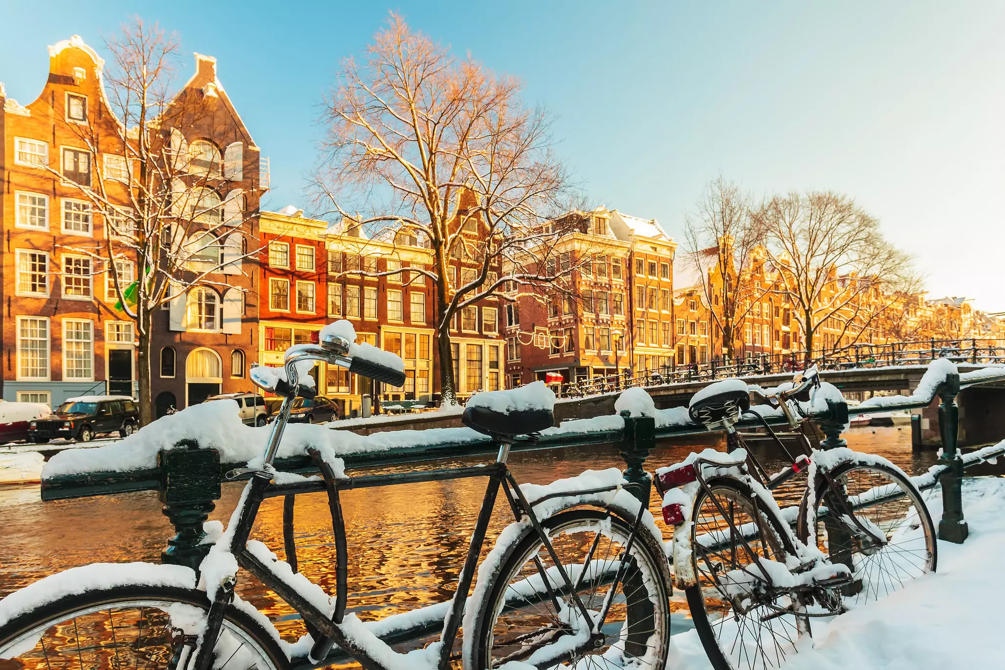 Bicycles covered with snow in front of a canal during winter in Amsterdam.