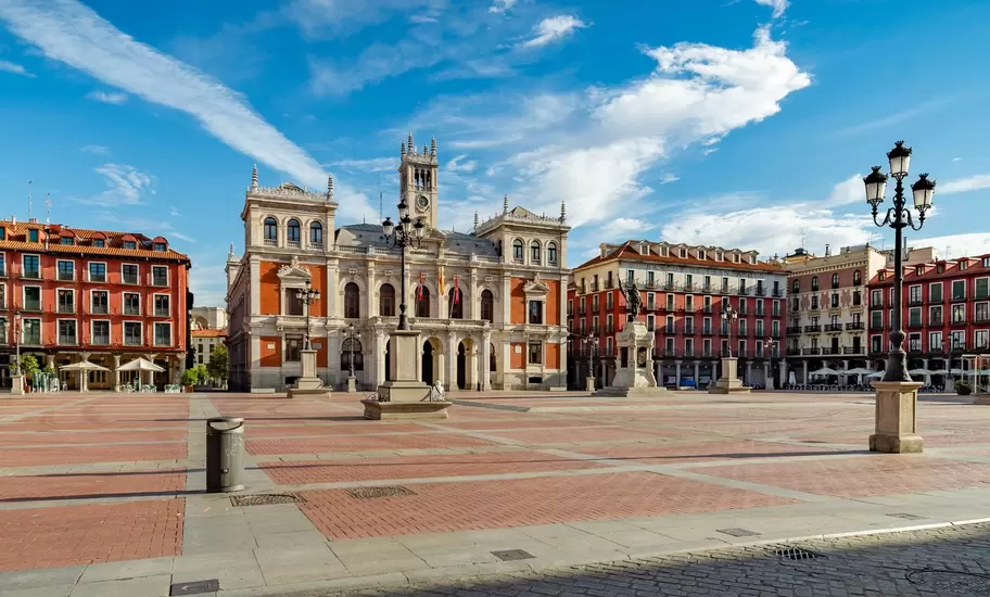 Plaza Mayor in Valladolid, Spain, a red-paved square ringed by red arcaded buildings, city hall and a statue at its centre