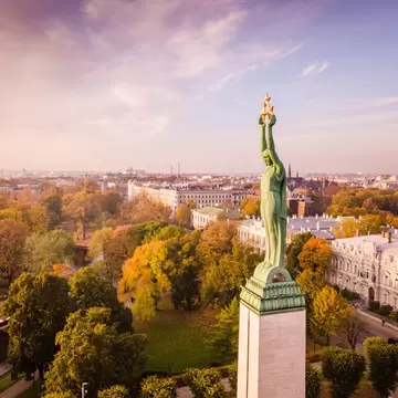Freedom Monument, Riga, from the air: green copper figure lifting three gilded stars above autumn trees and a canal