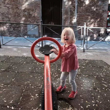 A child playing with one side of a see-saw in a city playground.