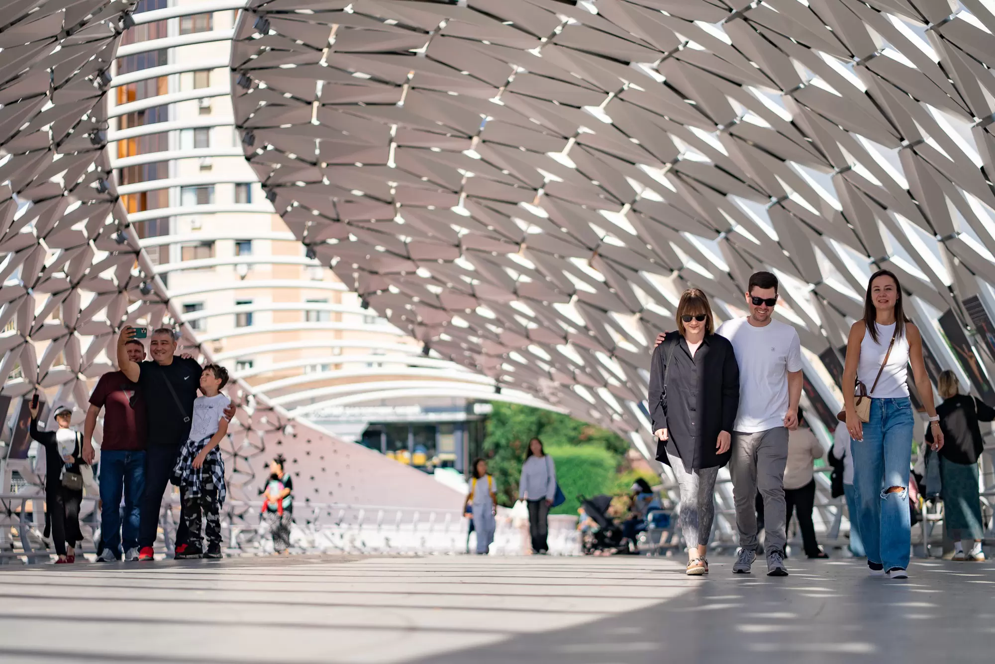 People walk on a pedestrian bridge in a city enveloped in lattice-like screens, Astana, Kazakhstan