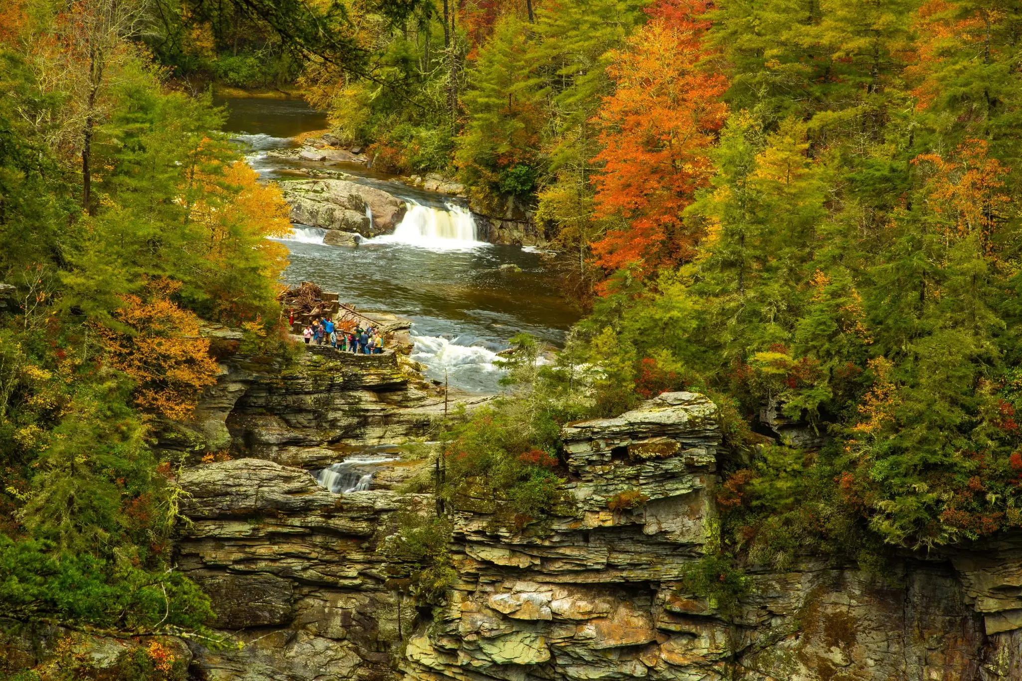 A wide view of people crowded on a small platform by a waterfall in a gorge, near the Blue Ridge Parkway, North Carolina