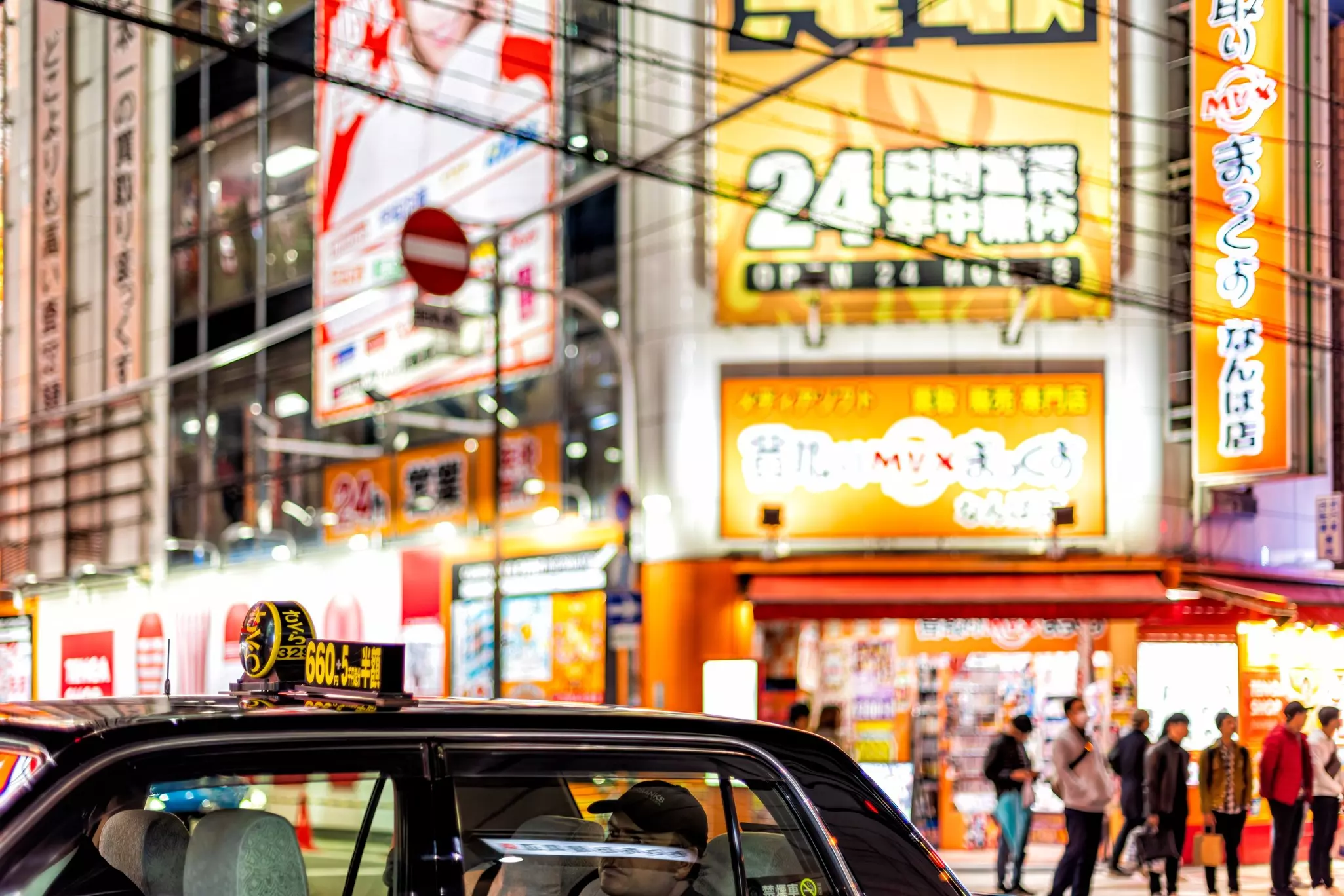 A taxi is pictured driving past buildings in a city illuminated with bright signage.