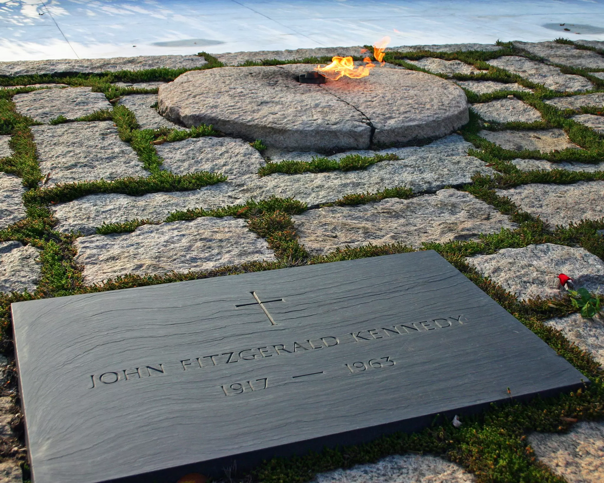 A black slab of stone with 'John Fitzgerald Kennedy' on it and the eternal flame in the background