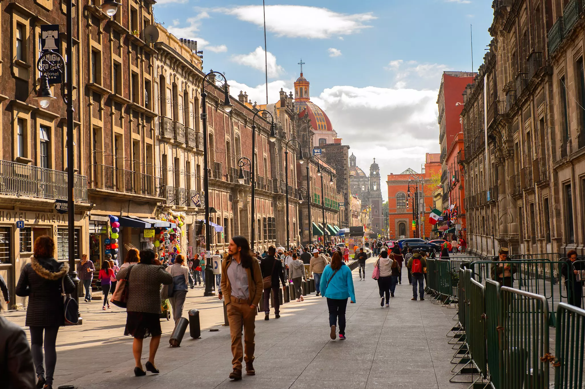 People walk down a pedestrianized street past historic buildings in a city.